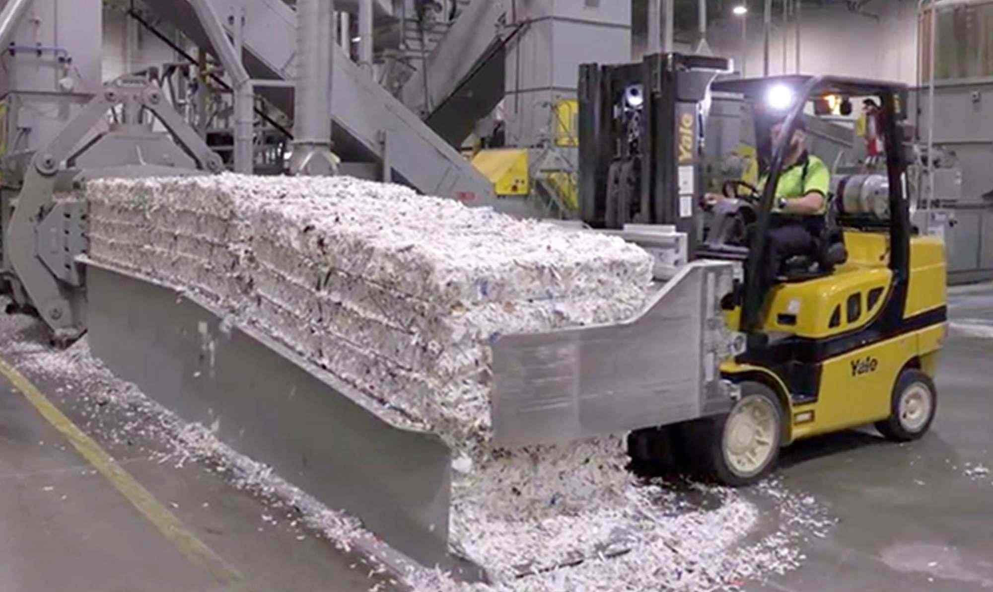shredded documents piled up in bulks lifted up by lifter operated by man